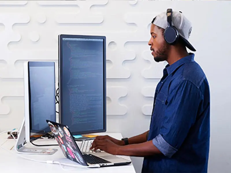 Focused software developer coding at a standing desk, wearing headphones for deep concentration.