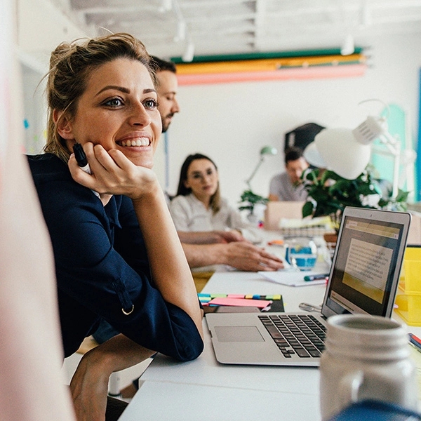 Smiling young woman in her office, with a colleagues working next to her