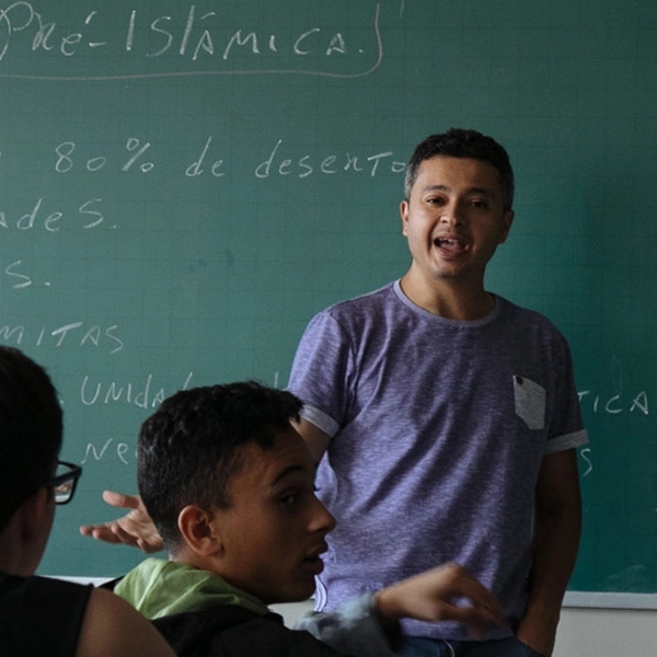Teacher stands in front of chalkboard explaining a topic to classroom