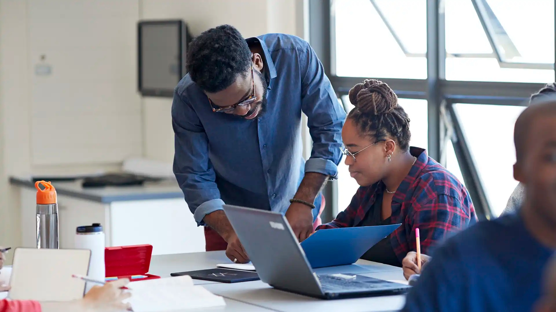 Teacher leaning over desk to assist student at laptop in classroom