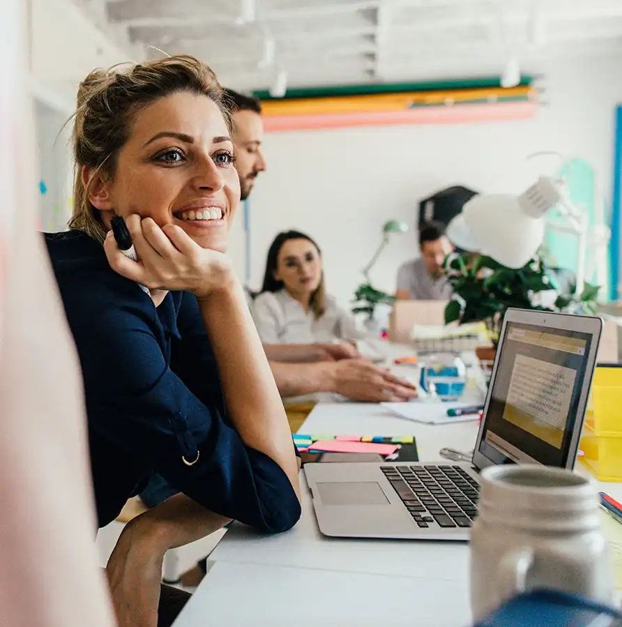 Smiling young woman in her office, with a colleagues working next to her