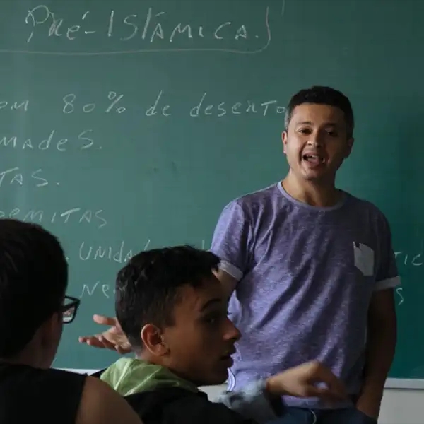 Teacher stands in front of chalkboard explaining a topic to classroom