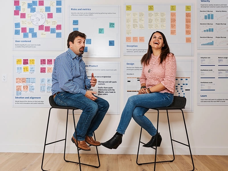 Two people sitting in front of sticky note boards presenting at a design thinking workshop