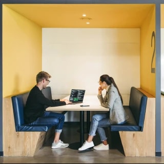 Two people work together at a table inside a study booth using a laptop
