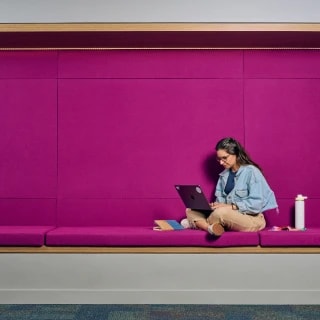 A woman sits with a laptop in a cushioned study nook, working independently.